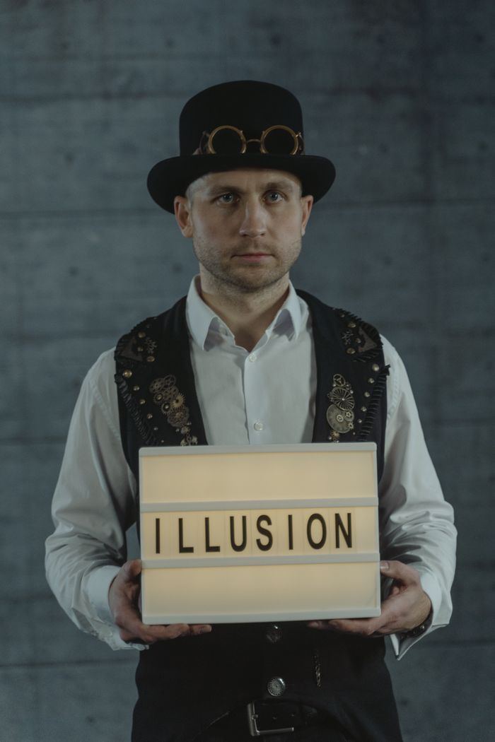 Mastering the First Impression: Your intriguing post title goes here A steampunk magician holding a sign spelling 'ILLUSION', set against a dark background indoors.